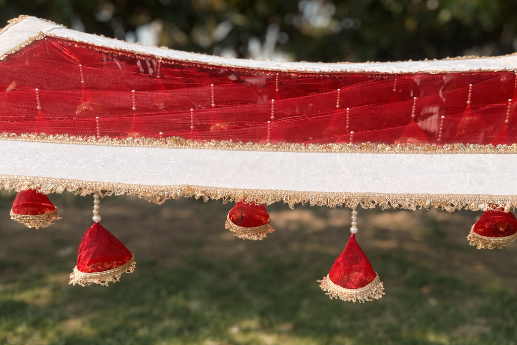 Decorative red fabric with gold trim and red hanging elements against a blurred green background