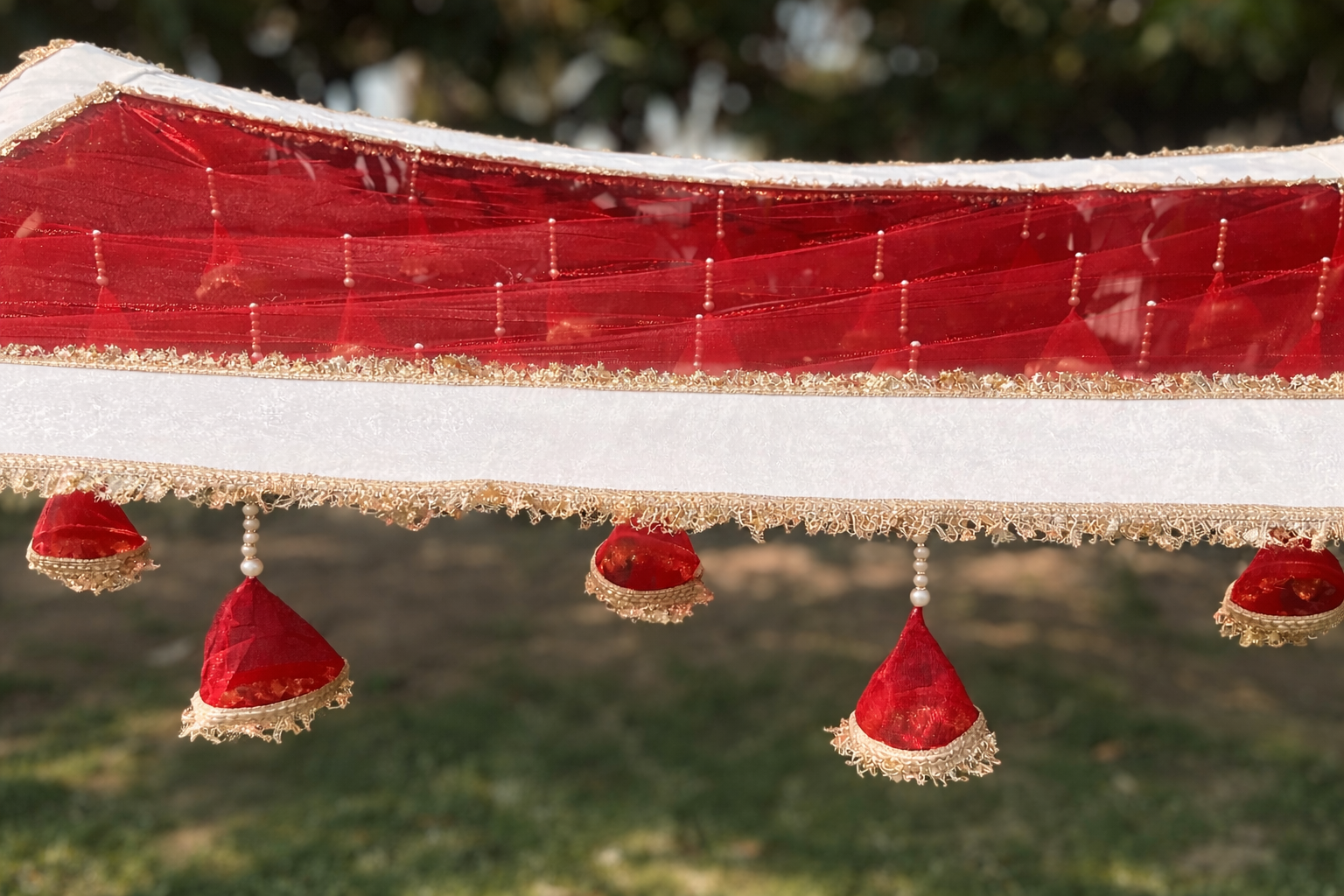 Decorative red fabric with gold trim and red hanging elements against a blurred green background