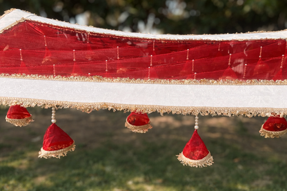 Decorative red fabric with gold trim and red hanging elements against a blurred green background