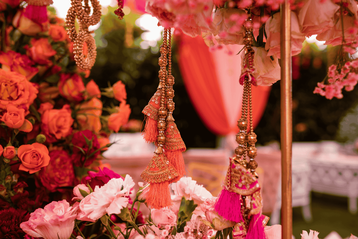 Decorative hanging jewelry with pink and gold elements amidst flowers and a blurred outdoor setting.