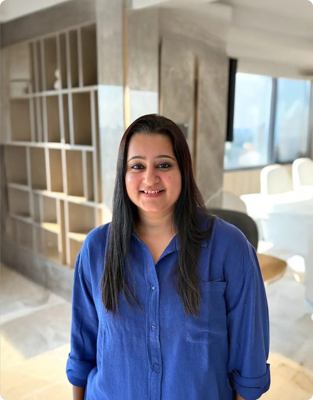 Woman in a blue shirt standing in a modern indoor setting with large windows.