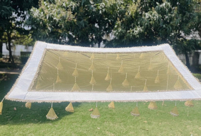 Decorative gold fabric with tassels on a grassy area with trees in the background