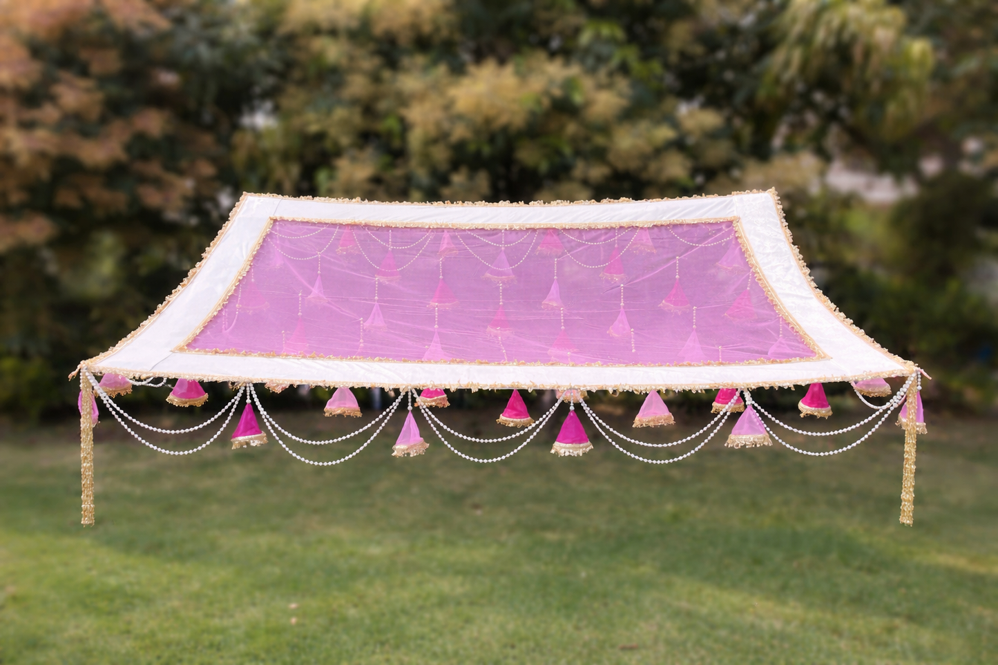 Decorative canopy with pink fabric and tassels on a grassy background