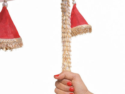 Decorative hanging plant with red and gold accents held by a hand with red nail polish on a white background