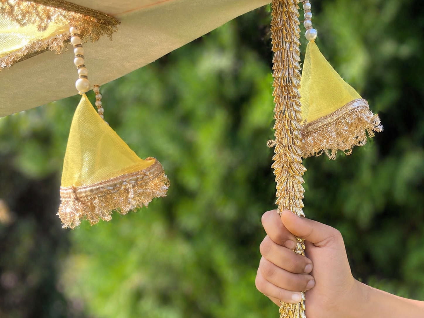 Decorative yellow and gold hanging elements held by a hand with a blurred green background