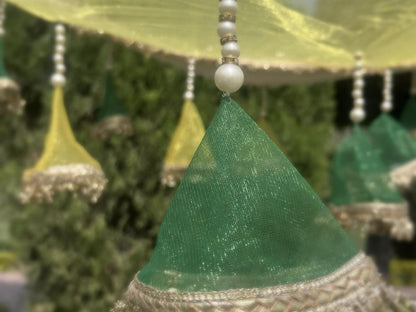 Decorative green cone-shaped object with beaded string against a blurred natural background