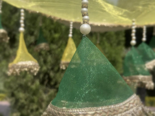 Decorative green cone-shaped object with beaded string against a blurred natural background