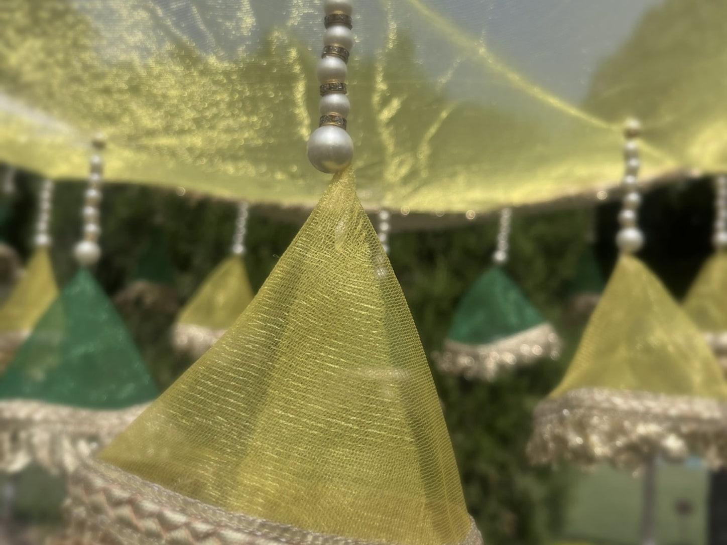 Green triangular fabric with silver trim hanging against a blurred natural background