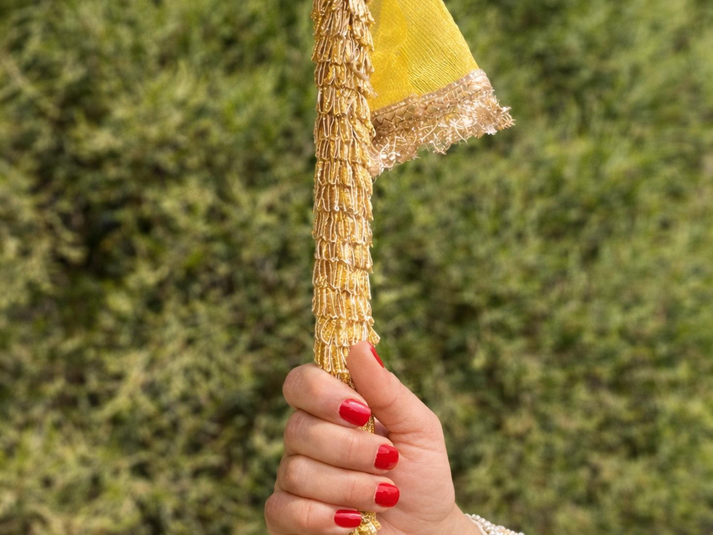 Hand holding a decorative gold and yellow object against a green background