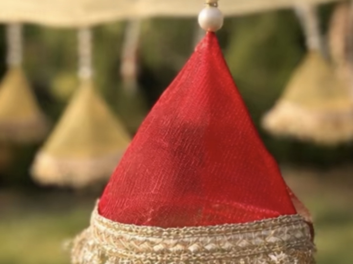 Decorative red cone-shaped object with gold base and pearl-like bead on a blurred natural background
