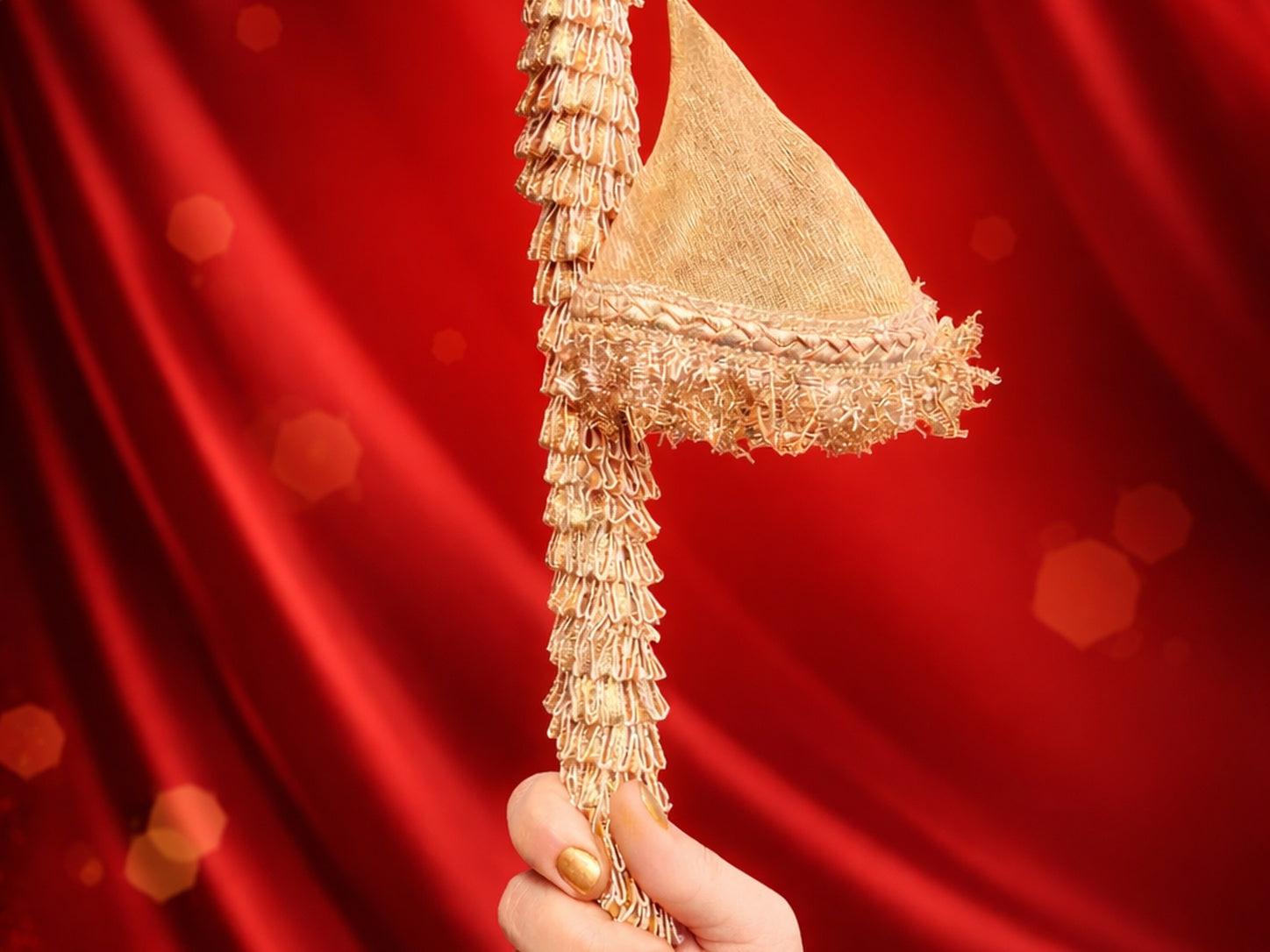 Gold decorative item held against a red curtain background
